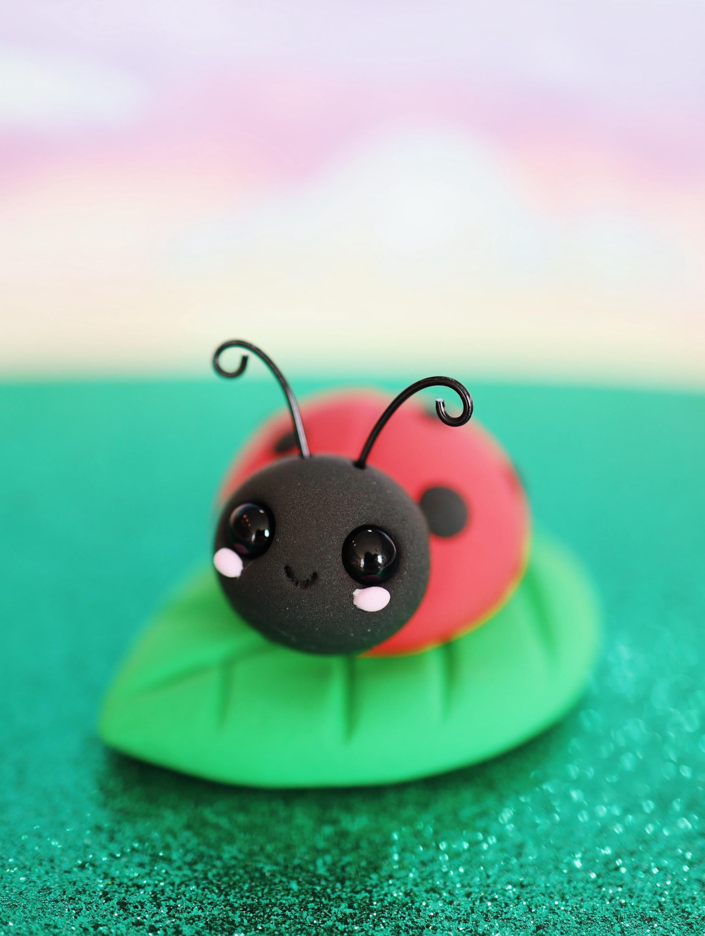 Cute ladybug figurine on a green leaf with a colorful gradient background