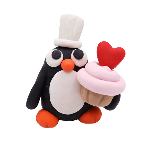 polymer clay penguin holding a pink cupcake with a red heart on a white background